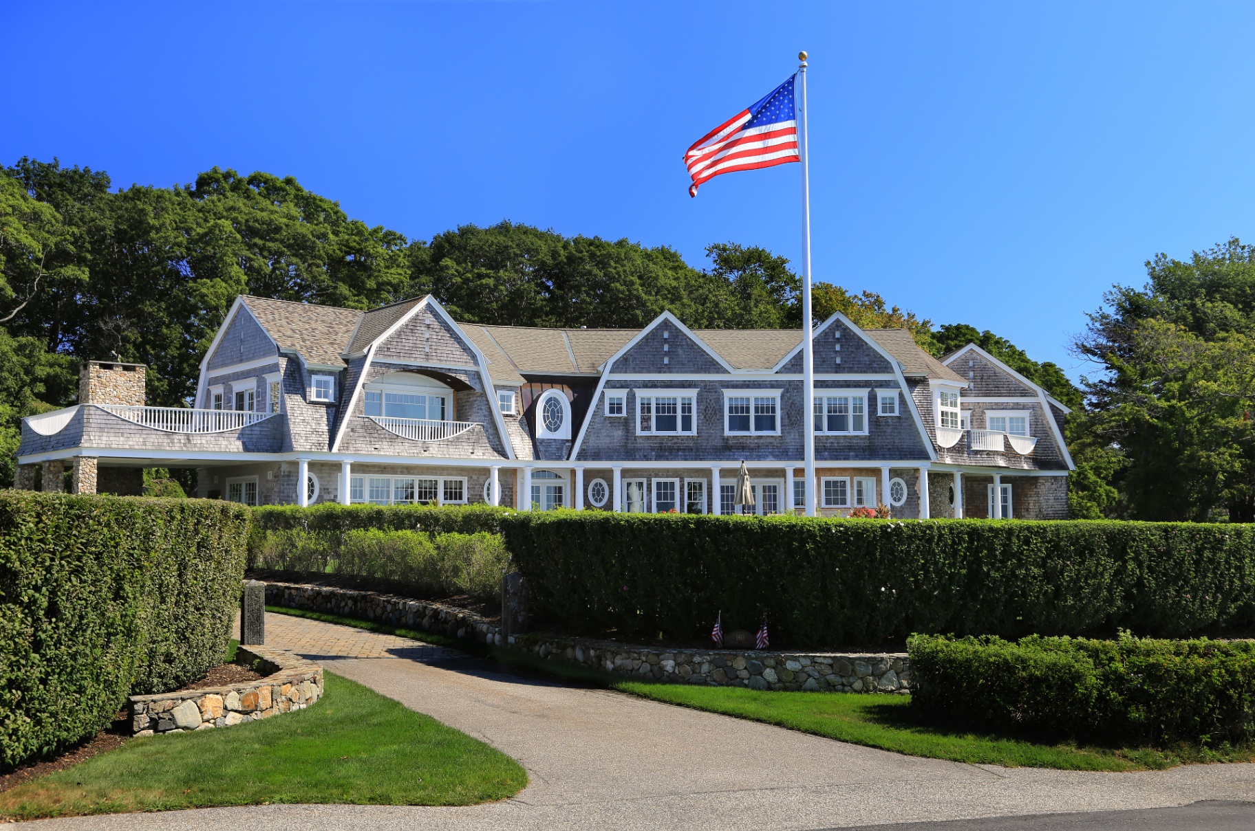 Classic New England shingle-style home with stone wall and American flag