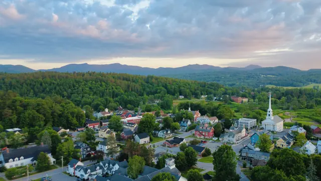 A Vermont village with a white church steeple below forested hills at sunrise